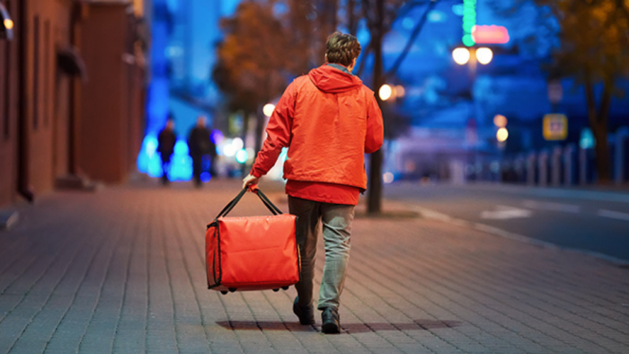 Delivery rider walking with red thermal bag on night city street