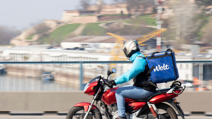 A courier working for Wolt food delivery service riding a scooter bike on the bridge over the Sava river with Kalemegdan fortress in the background