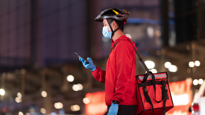 Delivery man wearing face protective mask to avoid corona virus Look at the phone to find the customer address through the application.