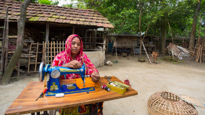 A middle-aged village woman sits in the backyard sewing for her family